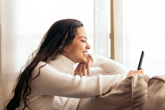 Connected at Home: Young Woman Sitting on Sofa Using Smartphone