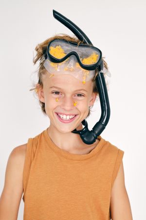 Happy boy in snorkeling goggles with petals off on light backgro
