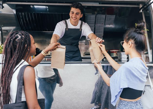 Women picking up meal in paper bag from smiling vendor