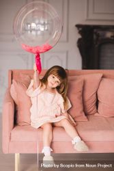 Young girl holding a balloon sitting on pink sofa 0WJvMb