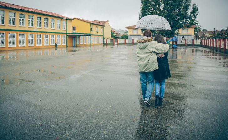 Back of couple walking under umbrella on rainy day