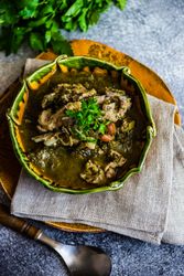 Top view of Georgian chakapuli stew on counter with fresh herbs and spoon