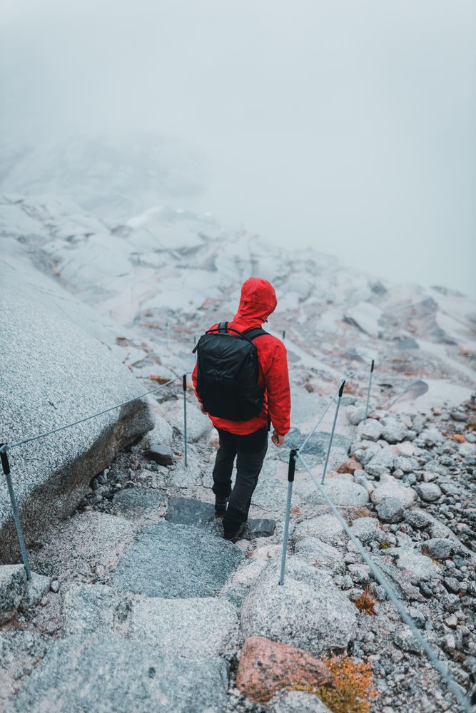 Back view of a man in red jacket with backpack walking on snow-covered staircase