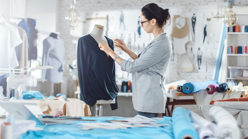Woman fashion, designer,  Working with Tailoring Mannequin, Adjusting Blouse. Her Studio is Bright and Sunny, Mannequins Standing around,