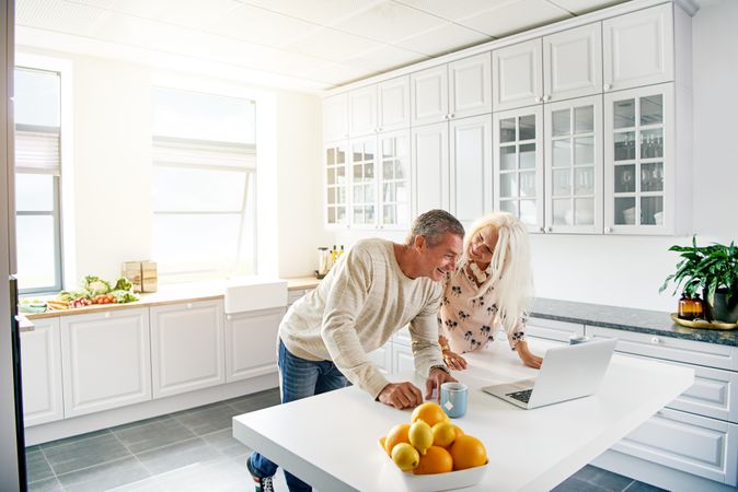 Older couple with a laptop and mugs of tea in their bright kitchen