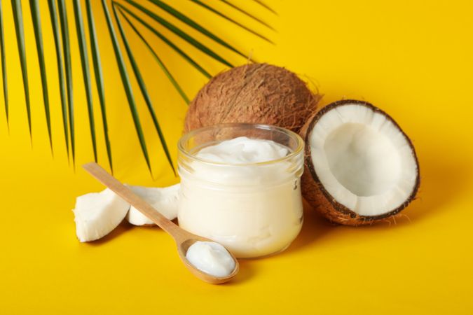 Coconut, cosmetics and palm branch on yellow background, close up
