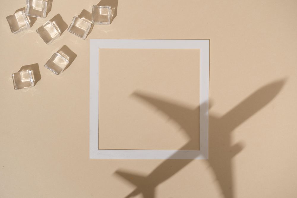 Shadow of airplane over beige paper background with square and ice cubes