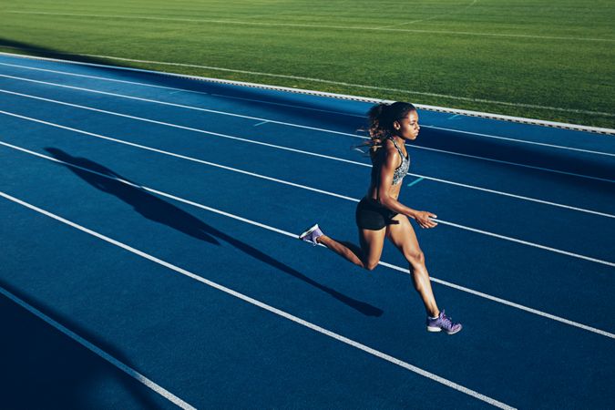 Outdoor shot of young woman athlete running on racetrack