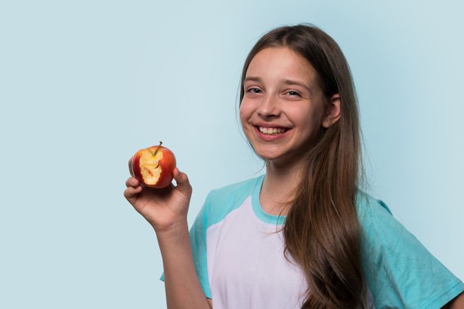 Young girl smiles brightly, holding an apple