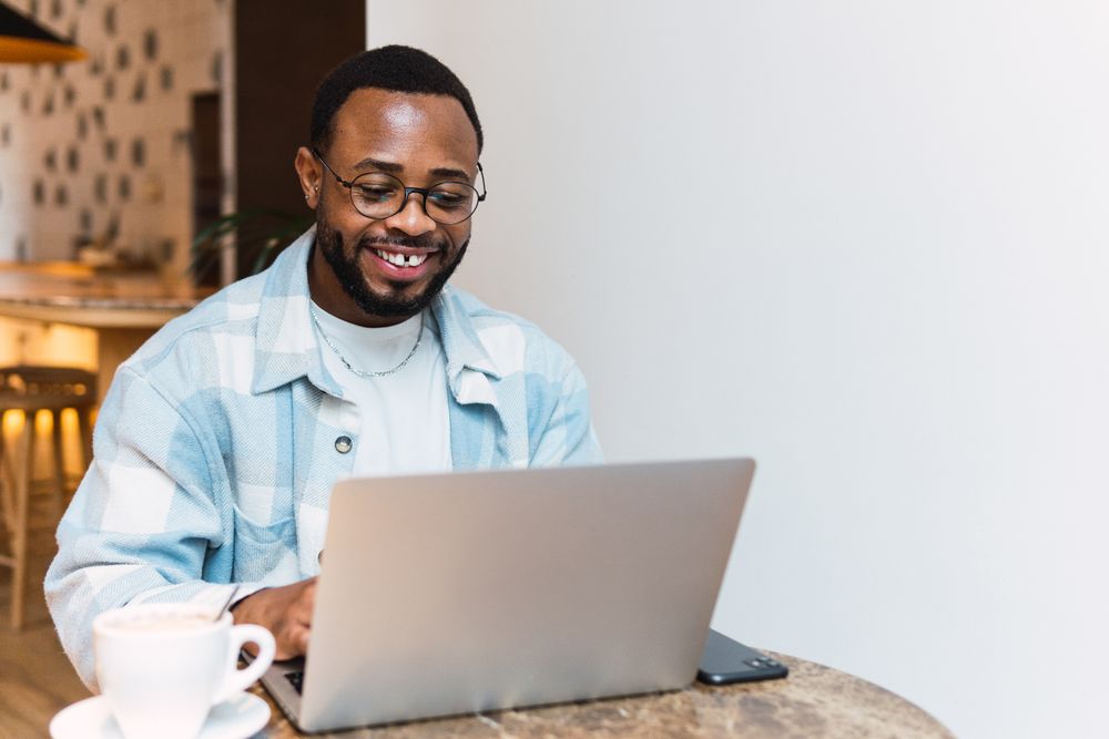 Delighted Black man with coffee browsing laptop