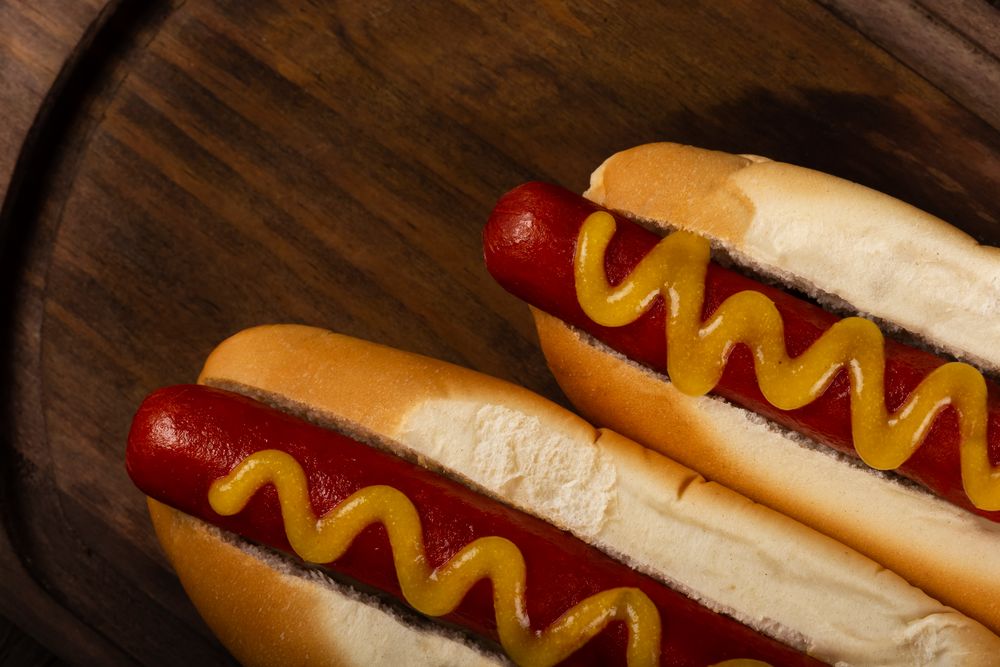 Top view of two hot dogs with mustard on wooden board