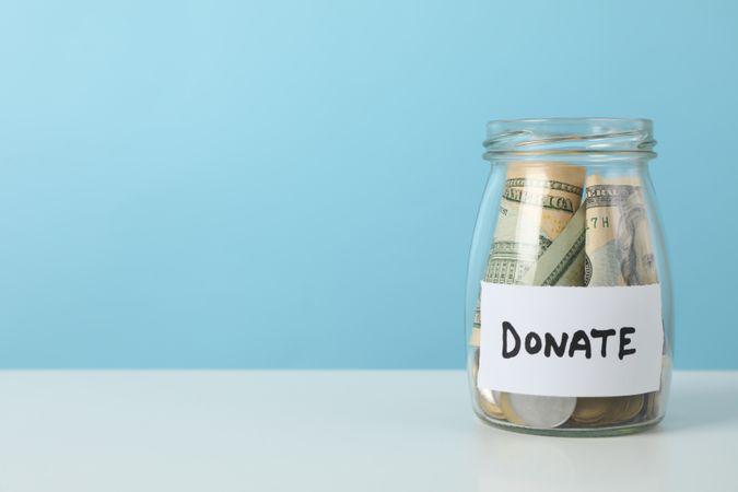 Glass jar with money and text Donate on table