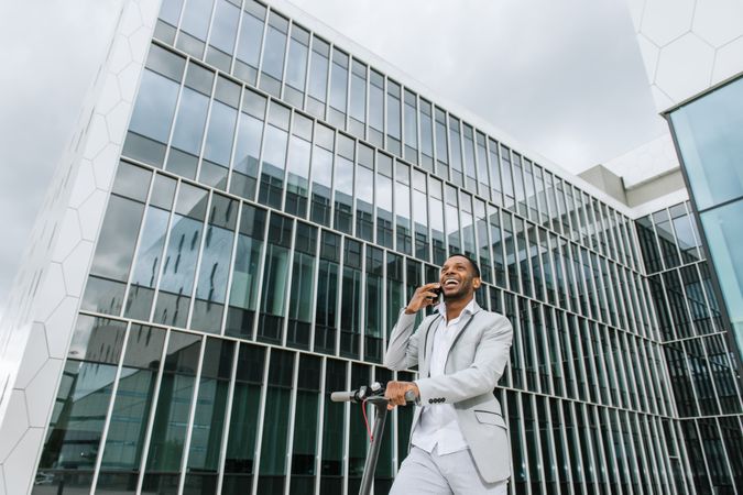 Smiling Black man riding scooter and speaking on smartphone