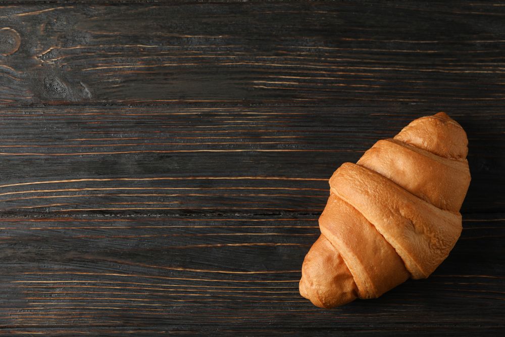 Tasty croissant on wooden background, top view and copy space