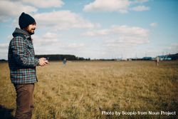 Side view of a man in plaid shirt holding a drone controller standing on grass field 5awBAb