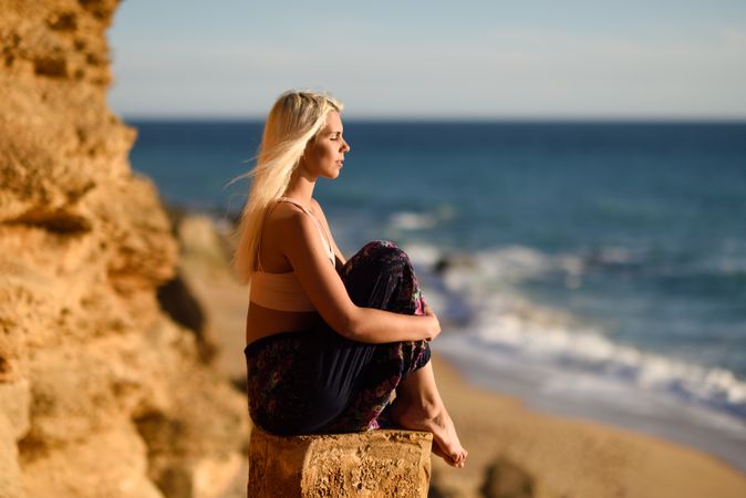 Blonde woman sitting on post over looking ocean