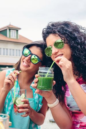 Two female friends sipping cocktails outside