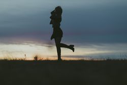Silhouette of woman with her leg kicked up behind her in a field at dusk