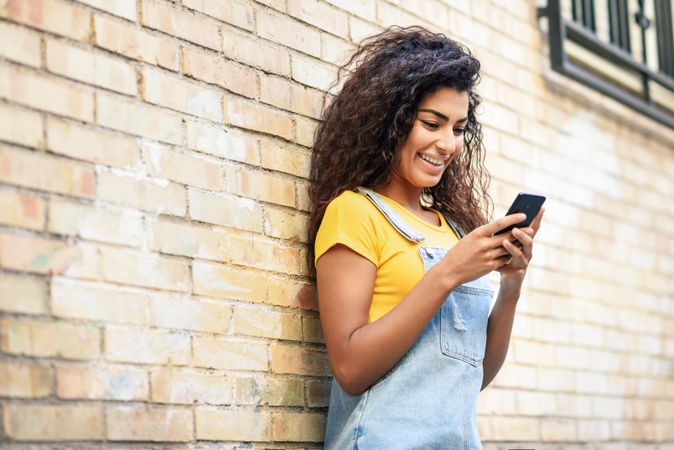 Arab woman texting with her smart phone outside in front of brick wall