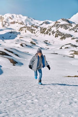 Cheerful boy running on snowy mountain slope