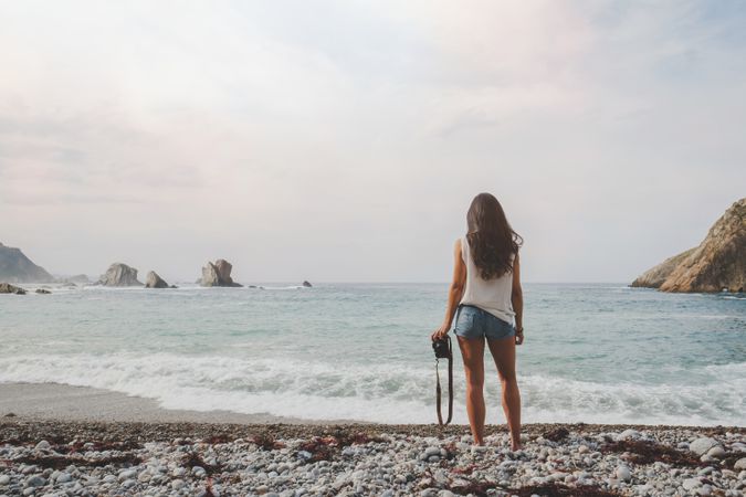 Woman with camera on shore near stones and water