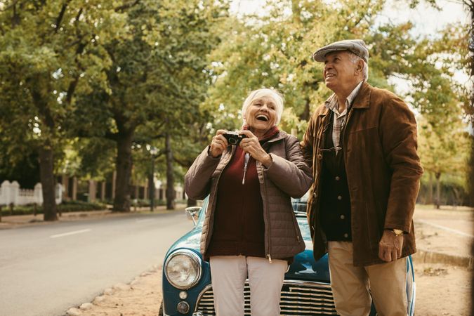 Cheerful older man and woman in warm clothes taking photographs their road trip