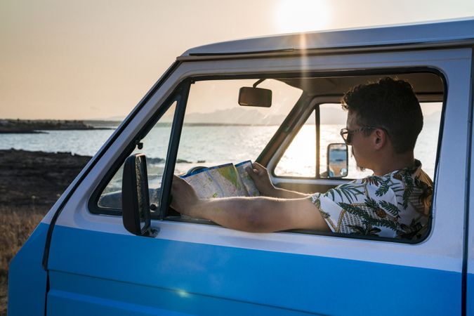 Adult man planing route for road trip while sitting in car on shore