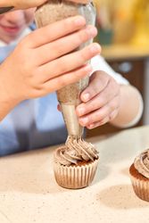 Crop girl decorating cupcakes with pastry bag