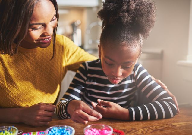 Black mother and daughter doing arts and crafts with beads at home