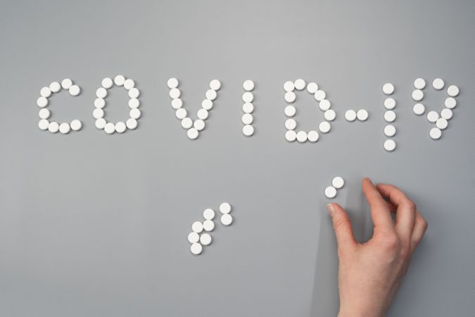 Cropped image of a person arranging pills to write "Covid-19"