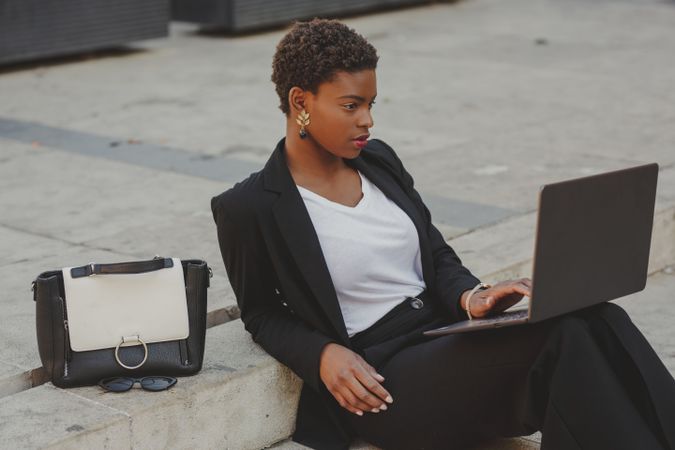 Stylish Black woman with laptop on steps near handbag