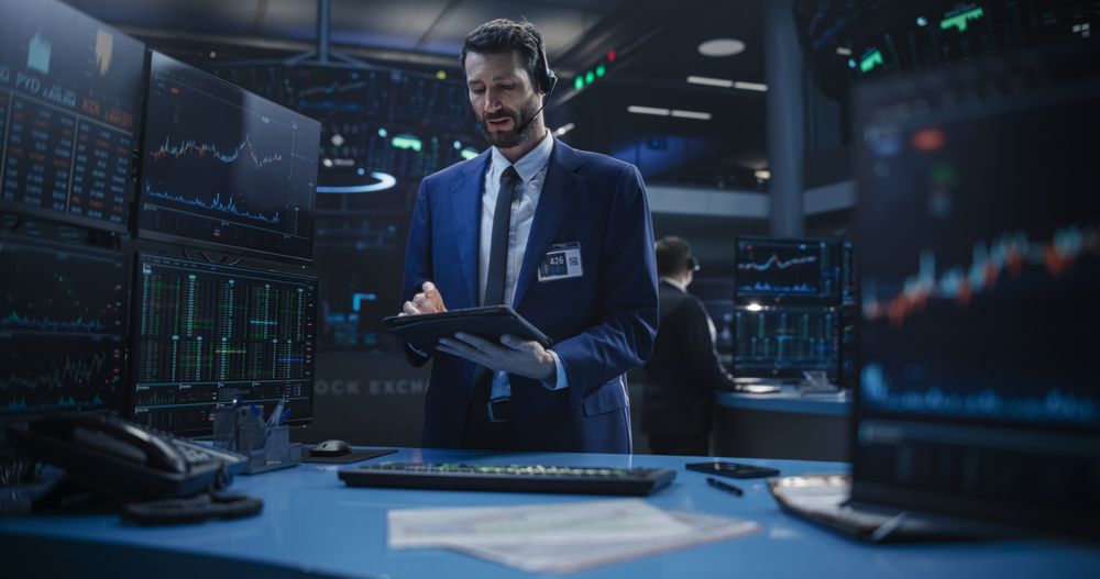 Portrait of a Young Handsome Stock Exchange Broker Working on a Tablet Computer, Researching Stocks Data, Analyzing Commodities and Exchange Market Charts.