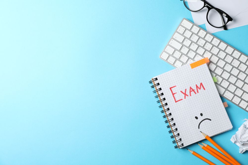Top view of exam notebook with drawn sad face on blue background with copy space
