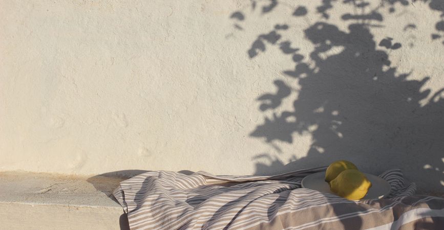 Mediterranean summer still life. Fresh lemons fruit in sunlight, floral foliage shadows overlay. Shabby old textured wall background. Cotton throw, blanket. Elegant neutral banner, vacation concept.