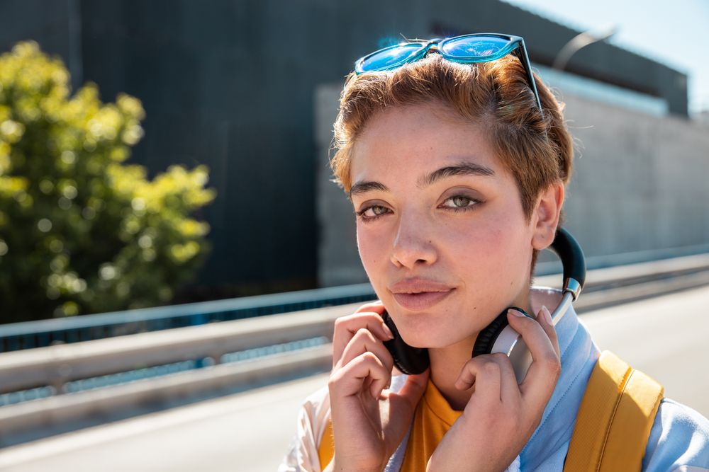 Playful trendy woman on street in sunshine covering camera with hands