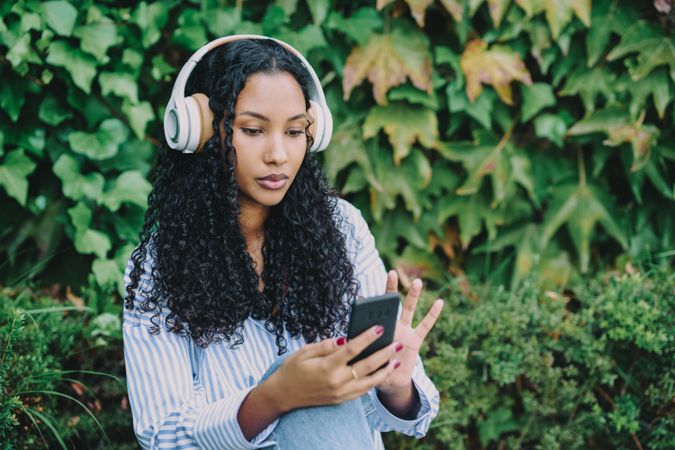 A Young Woman Immersed in Enjoying Music While Wearing Headphones in a Lush Green Setting Around Her