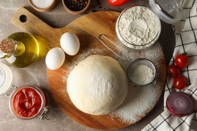 Dough and ingredients for cooking pizza on gray background