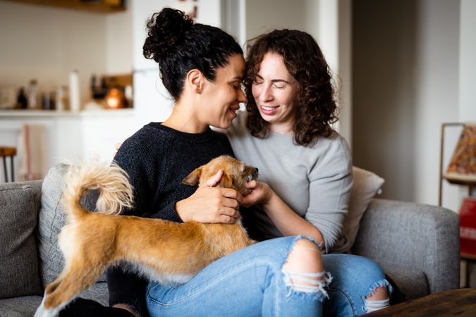 Female couple sitting close by and relaxing at home on sofa with dog