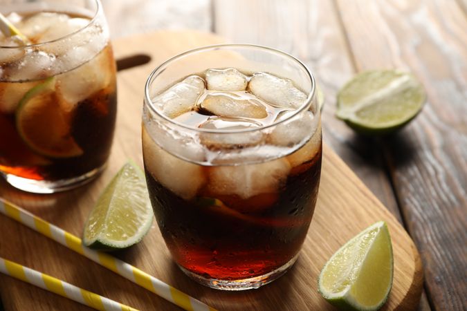 Glasses with ice cola, lime slices and tubules on wooden background