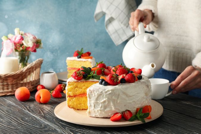 Woman pours tea on wooden table with berry cream cake. Tasty dessert
