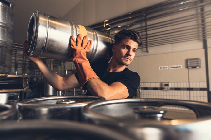 Handsome male worker moving beer keg while wearing rubber gloves