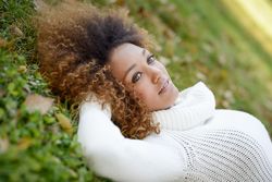 Smiling female in sweater lying down on park grass