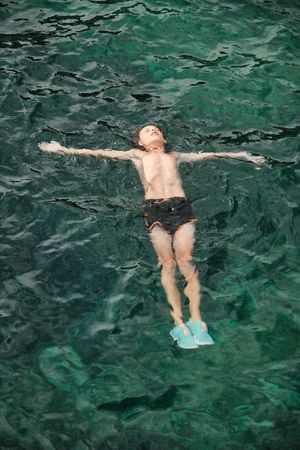 Shirtless boy floating and relaxing on sea water