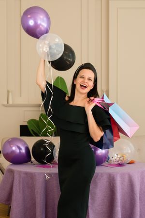 Woman joyfully posing with balloons and gift bags.
