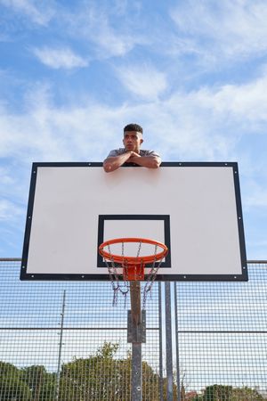 Male climbing on basketball backboard in outdoor sports ground