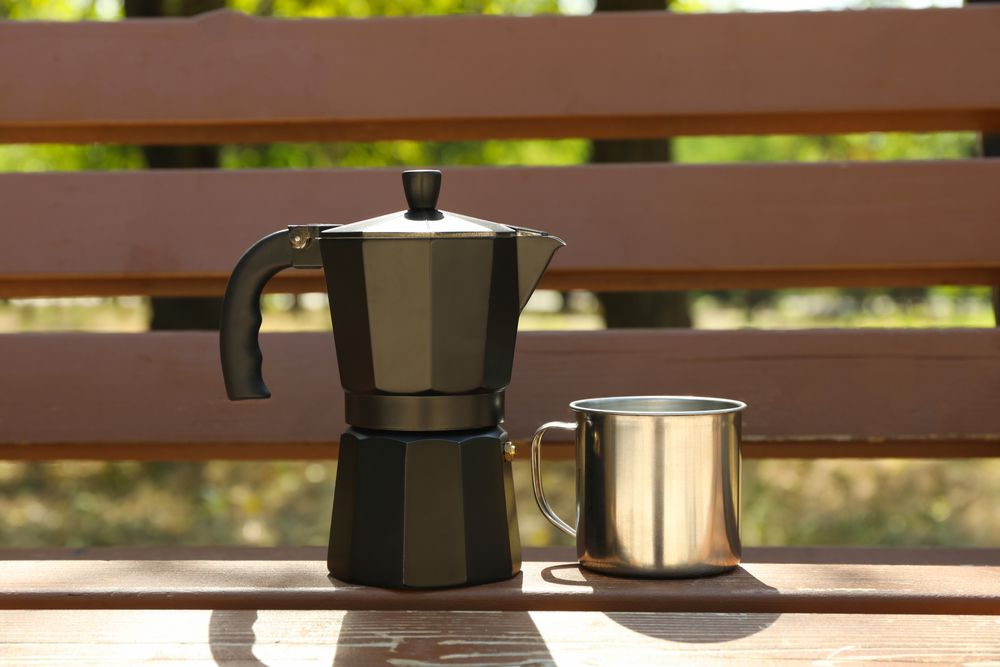 Coffee maker and metal cup on bench outdoor