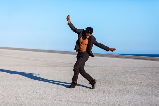 Front view of man standing outdoors with arms raised on sunny day