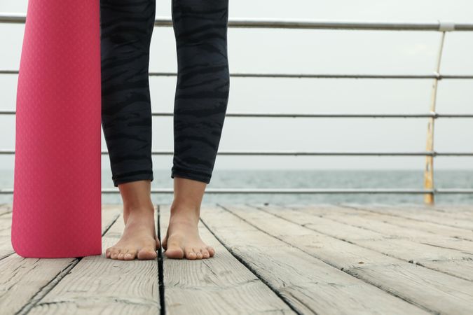 Female feet and yoga mat on wooden floor at sea, space for text