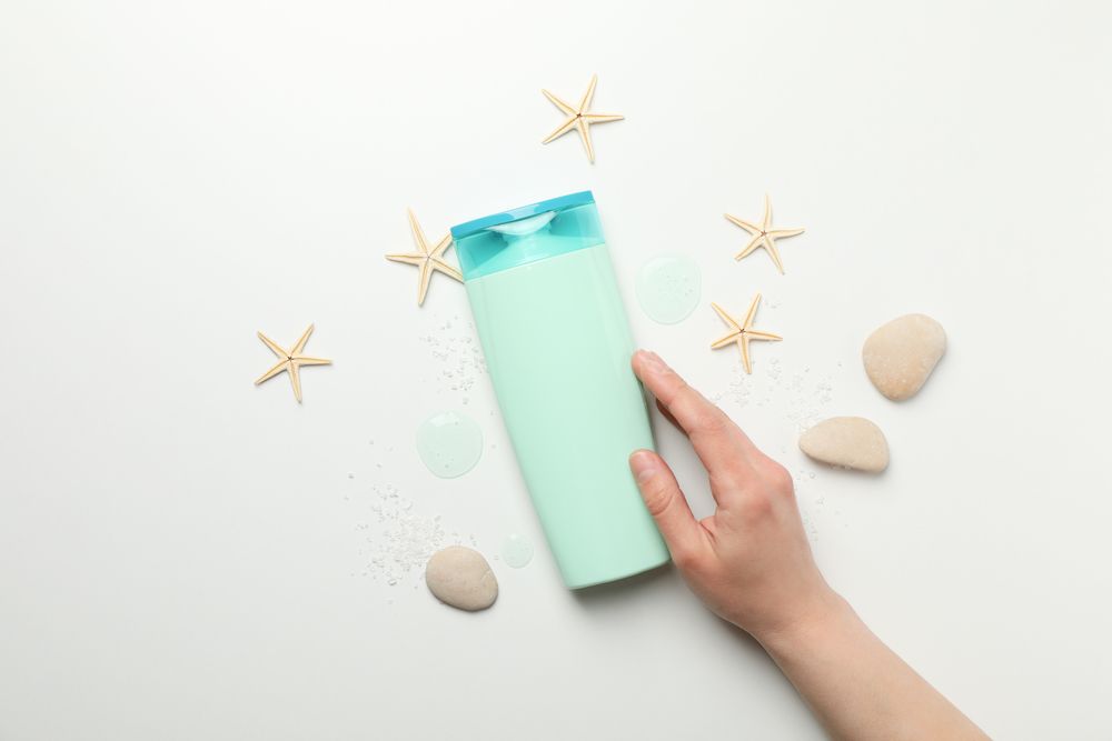 Female hand touches a bottle of shampoo on light background