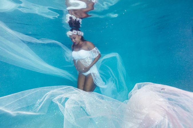 Pregnant woman in wreath and dress underwater